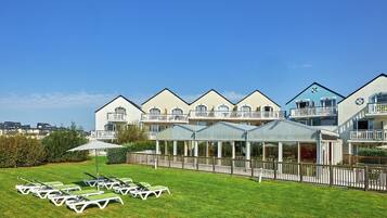 A hotel with multiple balconies, a covered outdoor seating area, and a well-maintained lawn.