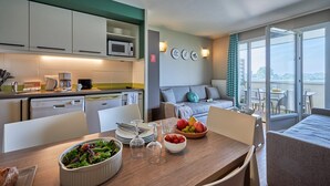 A modern kitchen with a dining area, a sofa, and a balcony with a view. - Stunning River View Apartment for 5 (COURSEULLES SUR MER)