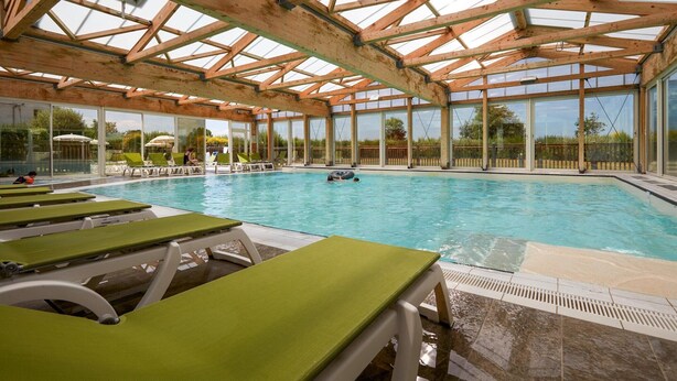 An indoor swimming pool with wooden beams, clear glass walls, and green lounge chairs. - Stunning River View Apartment for 5 (COURSEULLES SUR MER)