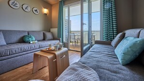 A modern living room with a sofa, a wooden side table, and a view of the outside. - Stunning River View Apartment for 5 (COURSEULLES SUR MER)