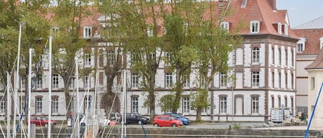 A marina with boats docked, a building with a red roof, and trees in the foreground.