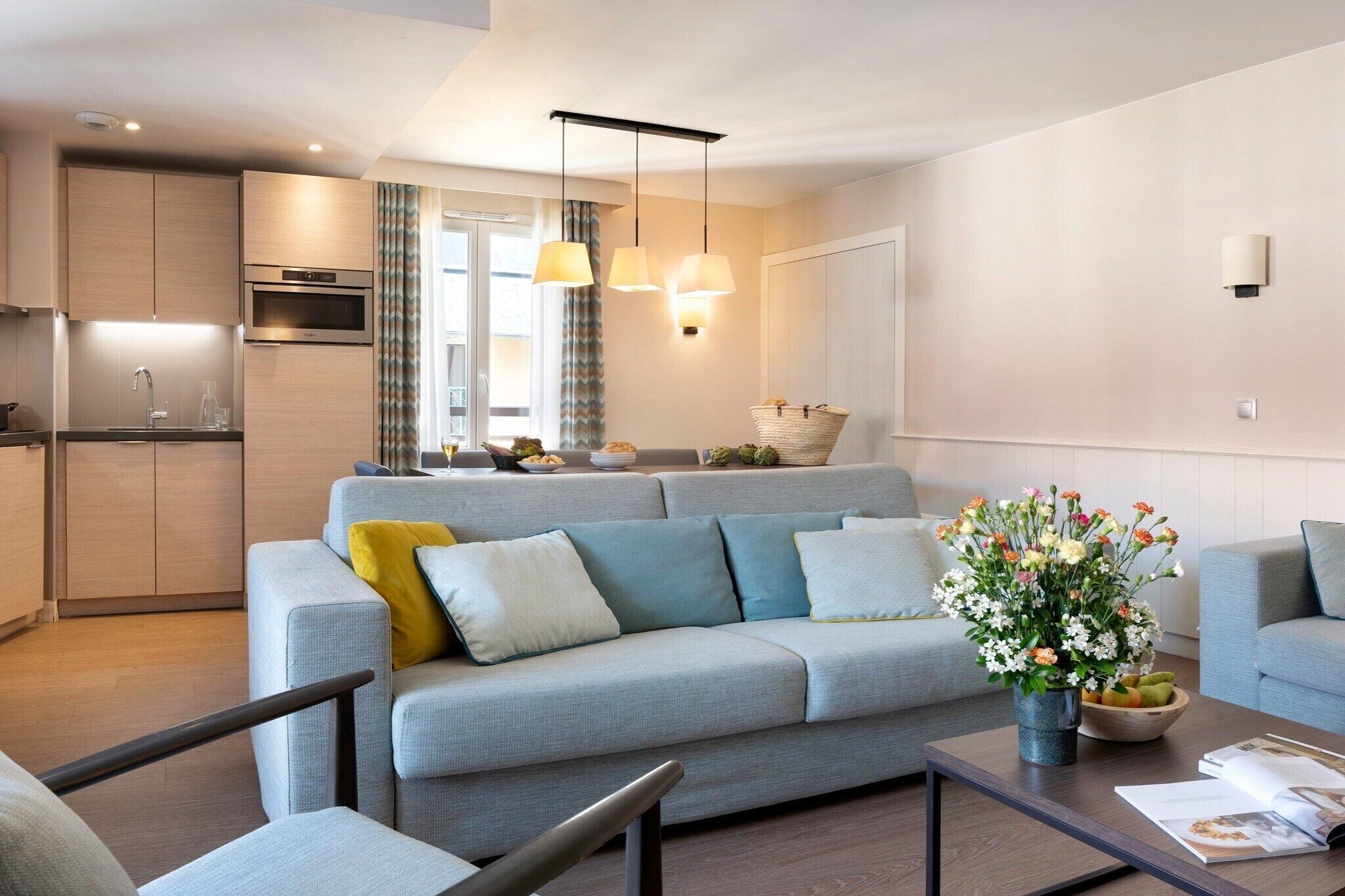 A modern living room with a sofa, coffee table, and a kitchen area in the background.