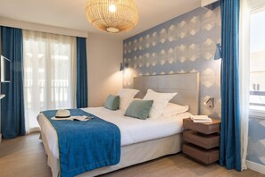 Una habitación de hotel moderna con una cama grande, una mesita de noche, un televisor montado en la pared y un ventanal con cortinas.