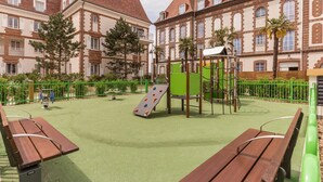 Un'area giochi con strutture di arrampicata e uno scivolo, circondata da panchine e una recinzione verde.