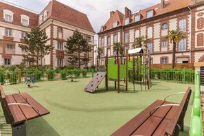 Ein Spielplatz mit Klettergerüsten und einer Rutsche, umgeben von Bänken und einem grünen Zaun.