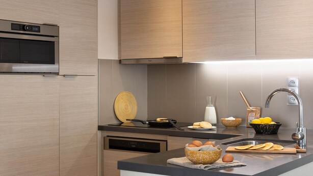 Una cucina moderna con forno integrato, forno a microonde, lavello e un piano di lavoro con diversi oggetti da cucina.
