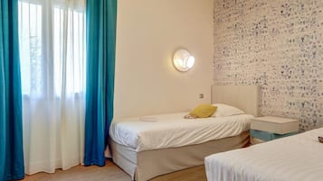 Une chambre à coucher comprenant un lit, une table de chevet, une commode, une fenêtre avec des rideaux et un mur décoré d’un motif.