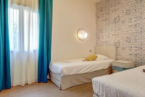 Ein Schlafzimmer mit einem Bett, einem Nachttisch, Vorhängen an einem Fenster und einer Wand mit Muster.