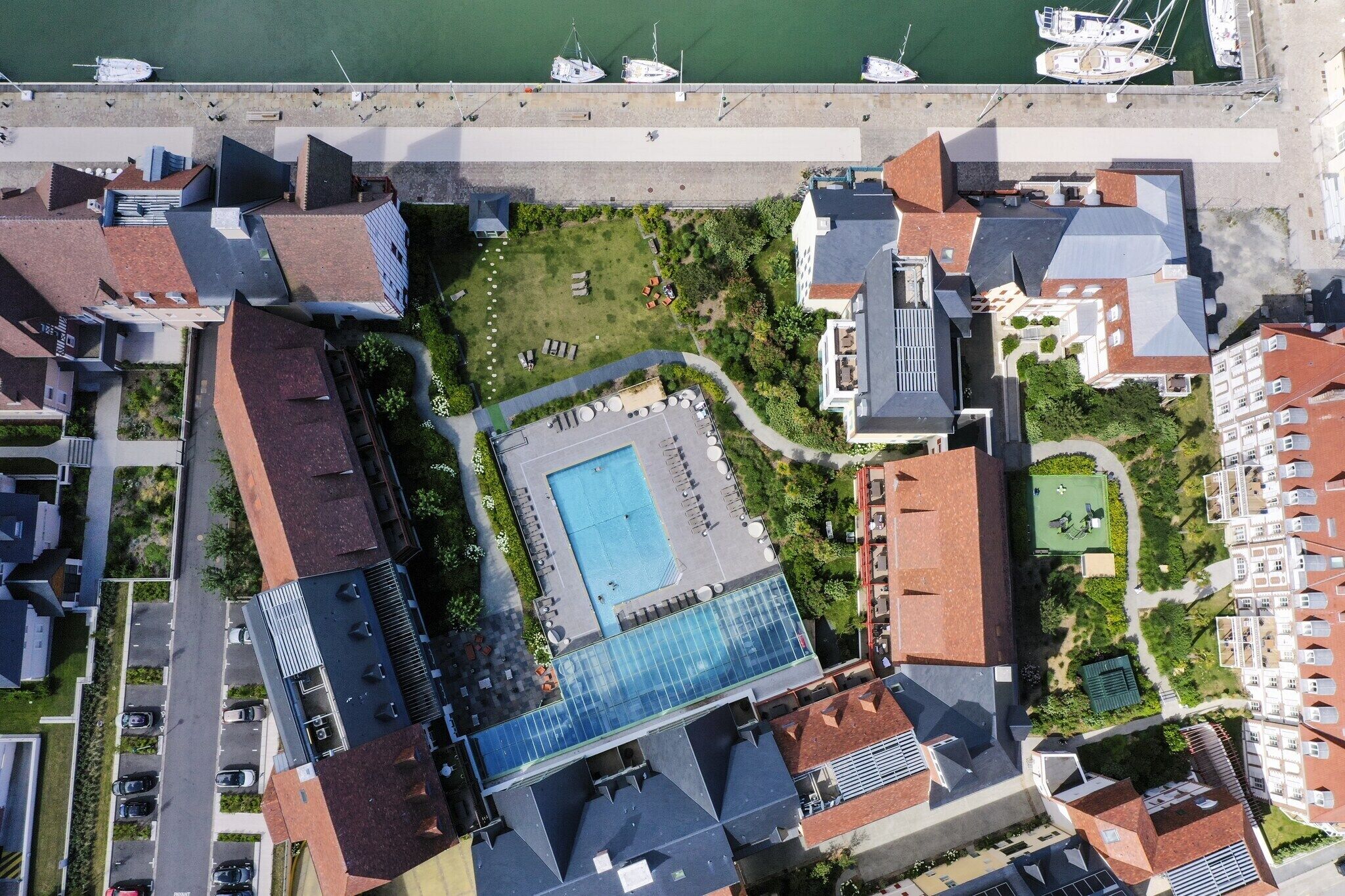 Luchtbeeld van een hotel met een zwembad, naast een jachthaven met boten.