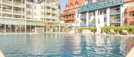 A swimming pool with a glass enclosure, surrounded by multi-story buildings with balconies.