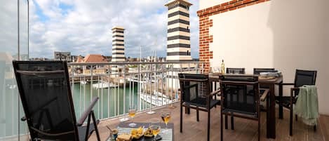 A balcony with a table set for dining, chairs, and a view of the marina with boats and buildings.