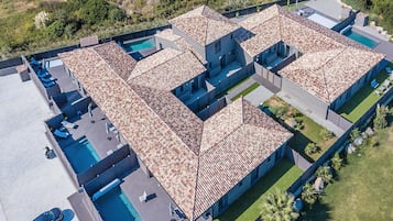 An aerial view of a modern resort with multiple swimming pools, a covered patio area, and a landscaped garden.