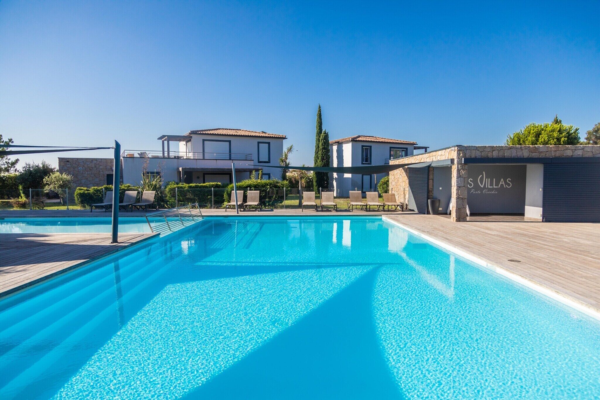 Ein Swimmingpool mit Liegestühlen, einer Steinmauer und einem Gebäude mit der Beschilderung 'S Villas'.
