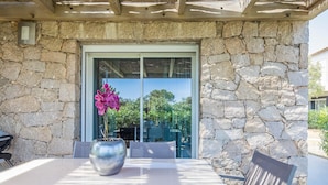 A stone exterior wall, a glass door, a table with chairs, and a potted plant. - Lecci Apartment with Outdoor Pool (Porto-Vecchio)