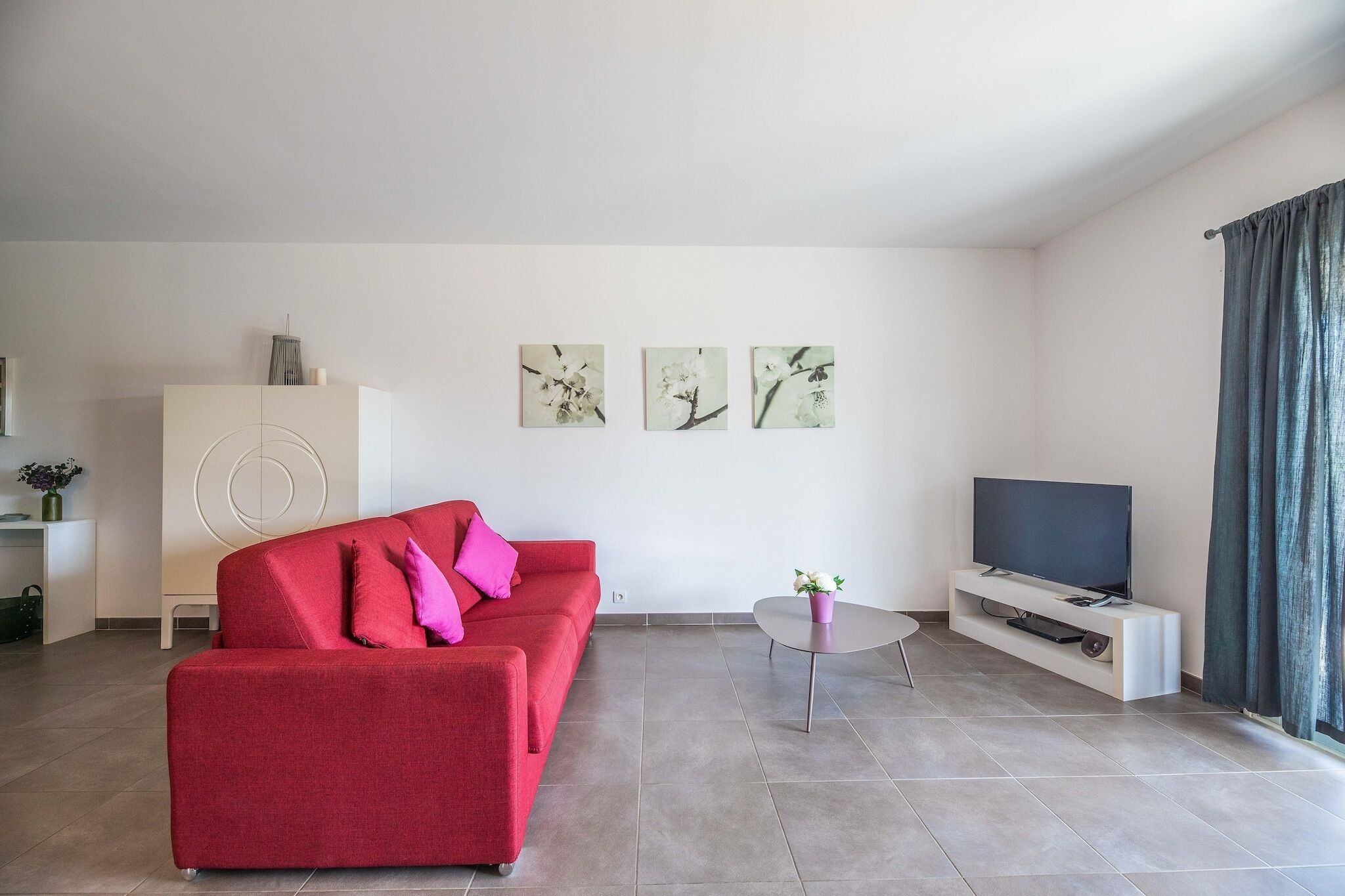 A modern living room with a red sofa, a TV on a stand, and three wall art pieces.