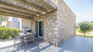 A covered outdoor seating area with a stone wall, a table with chairs, and a potted plant. - Corsican Flat with Pergola (Porto-Vecchio)