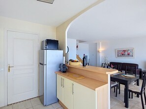 A compact kitchen with a refrigerator, microwave, and a dining area with a table and chairs. - Le Palais de la Mer by Interhome (Sainte Maxime)