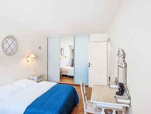 A bedroom with a bed, bedside table, lamp, mirror, and a wardrobe with a mirror. - Le Palais de la Mer by Interhome (Sainte Maxime)