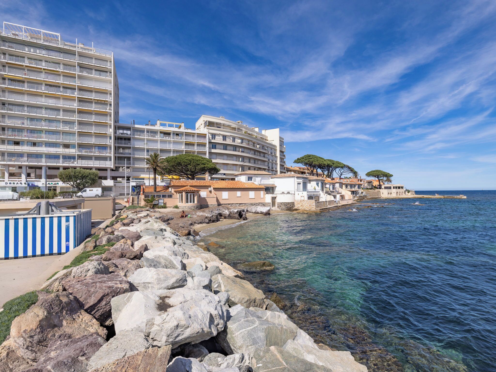Un hôtel situé sur la côte, avec plusieurs étages, un rivage rocheux et une eau d’un bleu cristallin.