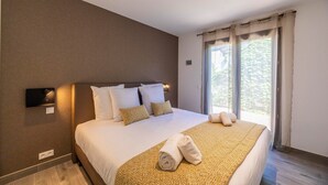 Une chambre d’hôtel avec un grand lit, une table de chevet, un téléviseur fixé au mur et une fenêtre avec des rideaux.
