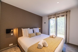 A hotel room with a large bed, a bedside table, a wall-mounted TV, and a window with curtains. - Lecci Apartment with Outdoor Pool (Porto-Vecchio)