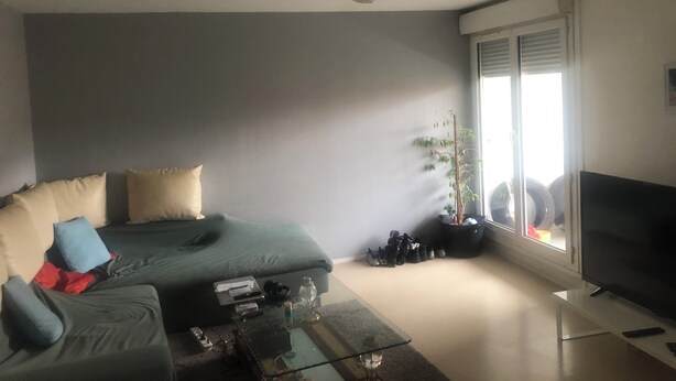 Una sala de estar con un sofá, una mesa de centro, un televisor y un amplio ventanal.