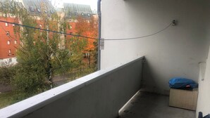 Un balcón con vistas a edificios y árboles, un enchufe y una bolsa azul sobre una mesita.