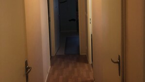 Un pasillo estrecho con suelo de madera, una puerta a la izquierda y otra a la derecha.