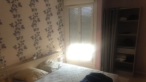 Un dormitorio con una cama, una ventana con persianas, un armario y una pared con estampado floral.