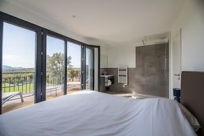 A bedroom with a large bed, a shower, a balcony with a view, and a bathroom with a sink and mirror. - Sun-Drenched Corsican Flat (Porto-Vecchio)