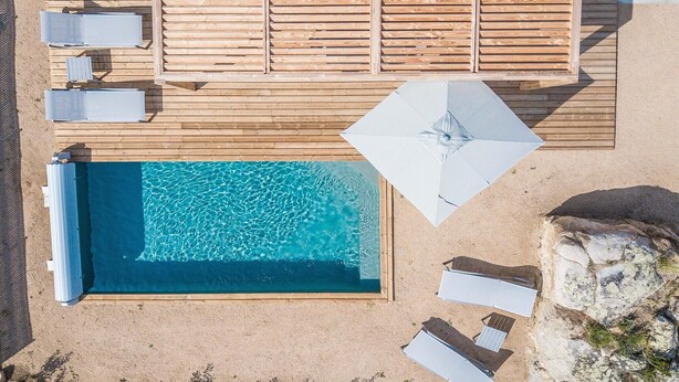Vue aérienne d’un espace piscine avec une terrasse en bois, des chaises longues et une piscine.
