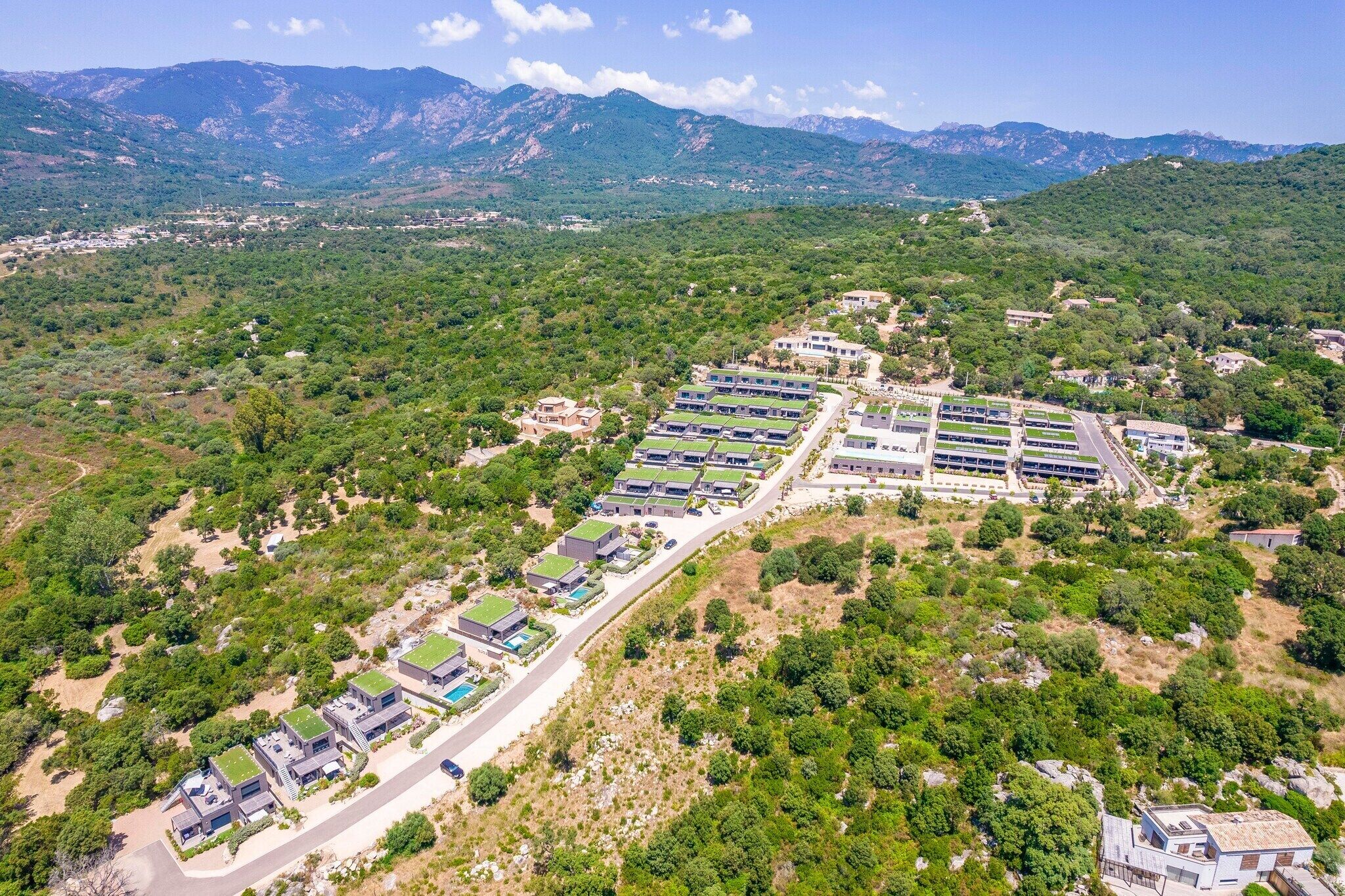An aerial view of a residential area with modern houses, a large building complex, and surrounding greenery.