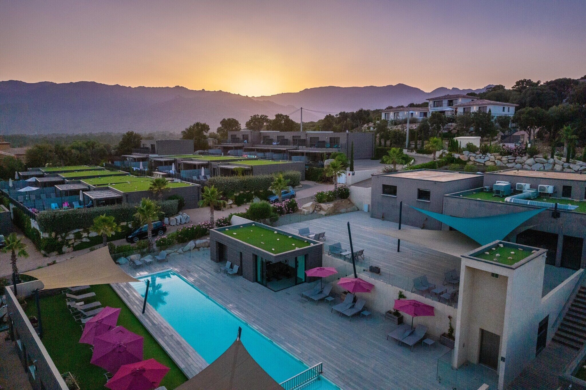 A resort with a swimming pool, lounge chairs, and a view of mountains.