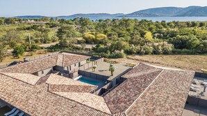 Un quartier résidentiel avec des toits recouverts de tuiles en terre cuite, une piscine et une vue sur un lac et des montagnes.