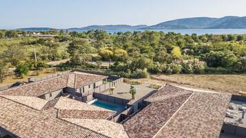 A residential area with terracotta-tiled roofs, a swimming pool, and a view of a lake and mountains.