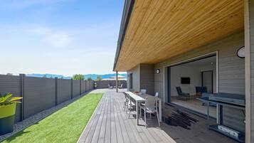 Un patio moderno al aire libre con terraza de madera, una mesa de comedor con sillas y un área de estar con sofá y butacas.