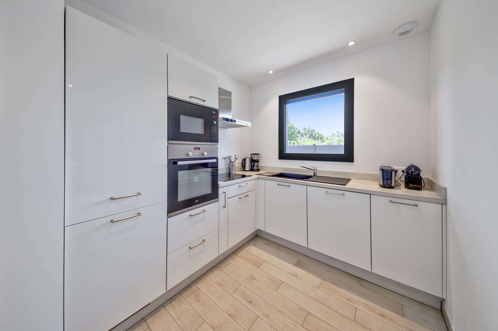 A modern kitchen with white cabinets, a built-in oven, microwave, and coffee maker.