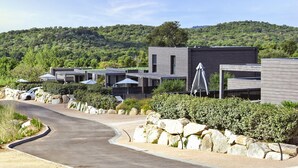 Ein modernes Resort mit mehreren Blockhütten, einer Serpentinenstraße und einem bewaldeten Hang im Hintergrund.