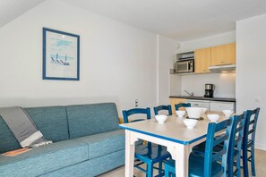 Ein gemütlicher Wohnraum mit Küchenzeile, einem Esstisch mit Stühlen, einer Couch und einem gerahmten Bild an der Wand.