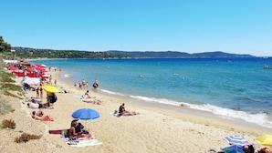 A beach with people sunbathing and swimming, red umbrellas, and a clear blue sky. - in Cavalaire-sur-Mer by Interhome (Cavalaire)