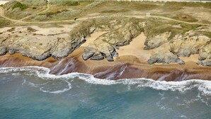 Ett kustlandskap med branta klippor, en sandstrand och fri utsikt över havet.