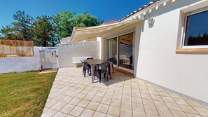 Eine Terrasse mit Tisch und Stühlen, eine Schiebetür und eine weiße Außenwand.