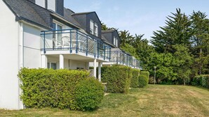 Ein modernes, zweistöckiges Haus mit Balkon, umgeben von gepflegten Hecken und einem Rasen.
