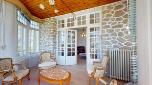 Ein Zimmer mit Steinwänden, Holzboden und großen Fenstern. Es gibt zwei Polsterstühle und einen runden Tisch.