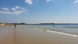 Ein Strand mit klarem Himmel, ruhigem Wasser und ein paar Personen, die am Ufer entlanggehen.