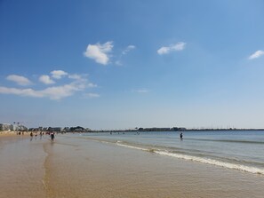 Ein Strand mit klarem Himmel, ruhigem Wasser und ein paar Personen, die am Ufer entlanggehen.