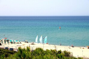 Ein Strand mit freiem Blick auf das Meer, mehreren Sonnenschirmen und einigen Personen.