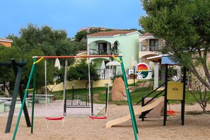 Ein Spielplatz mit Schaukeln, einer Rutsche und einer Kletterkonstruktion.