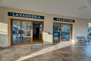 Ein Gebäudeeingang mit Schildern 'LAVANDERIA' und 'RECEPTION', einer Bank und einem gefliesten Boden.