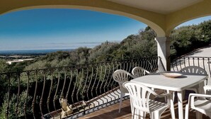 Ein Balkon mit weißen Stühlen und einem Tisch, der auf eine malerische Landschaft mit Bäumen und einer entfernten Aussicht blickt.